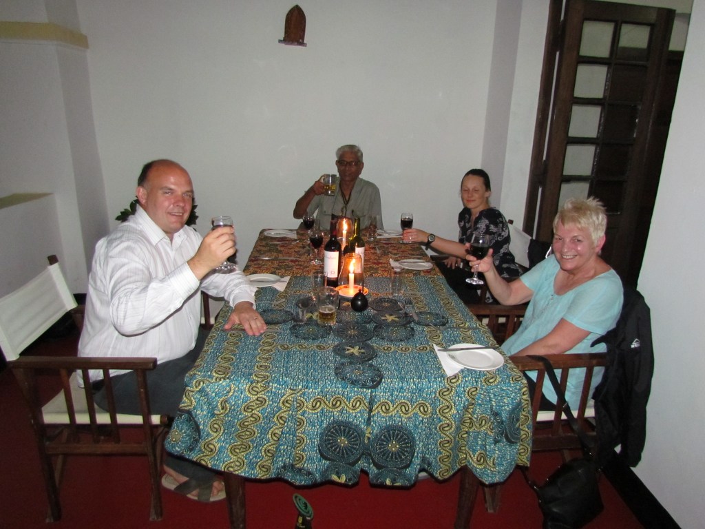 Group of four people sitting around a decorated table in a dimly lit setting, each holding a drink and smiling.